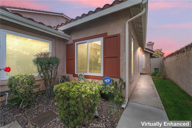 view of side of home featuring a tiled roof, stucco siding, and fence