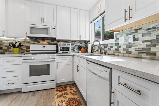 kitchen with a sink, white appliances, backsplash, and white cabinets