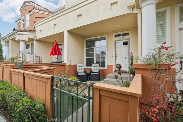 entrance to property with a gate, covered porch, stucco siding, and fence