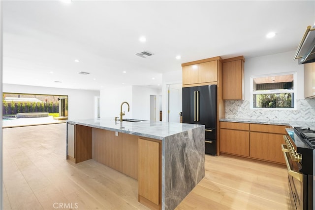 kitchen with visible vents, a sink, premium appliances, tasteful backsplash, and light stone countertops