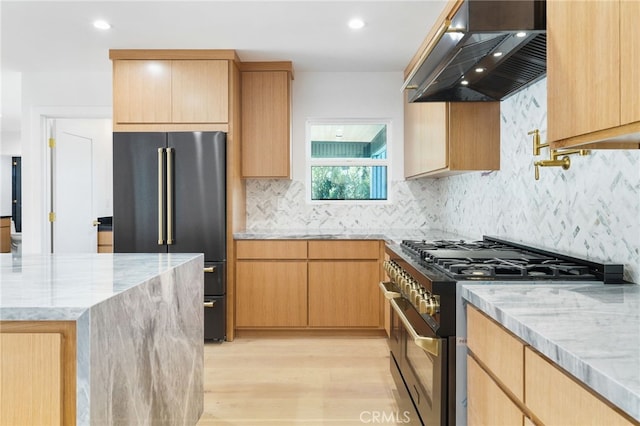 kitchen featuring light stone counters, light wood finished floors, decorative backsplash, wall chimney range hood, and high quality appliances