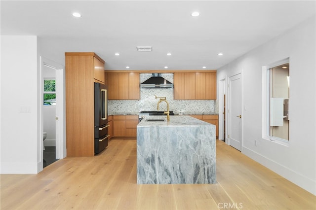 kitchen featuring light stone counters, visible vents, light wood-style flooring, high end black refrigerator, and wall chimney range hood