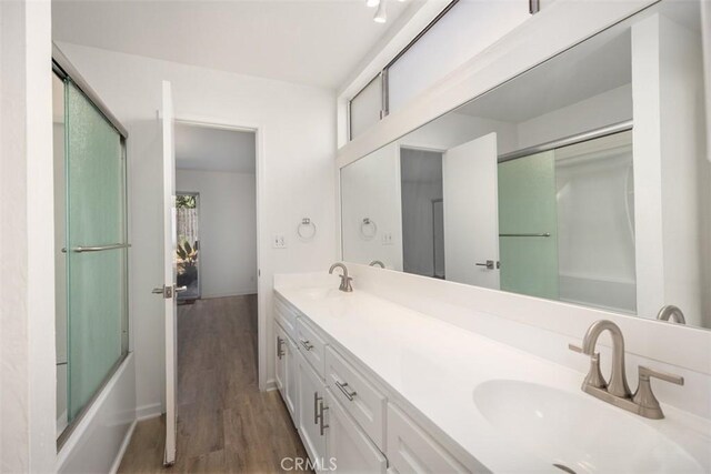 bathroom with a sink, enclosed tub / shower combo, wood finished floors, and double vanity