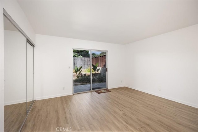 unfurnished bedroom with a closet, baseboards, wood finished floors, and access to outside