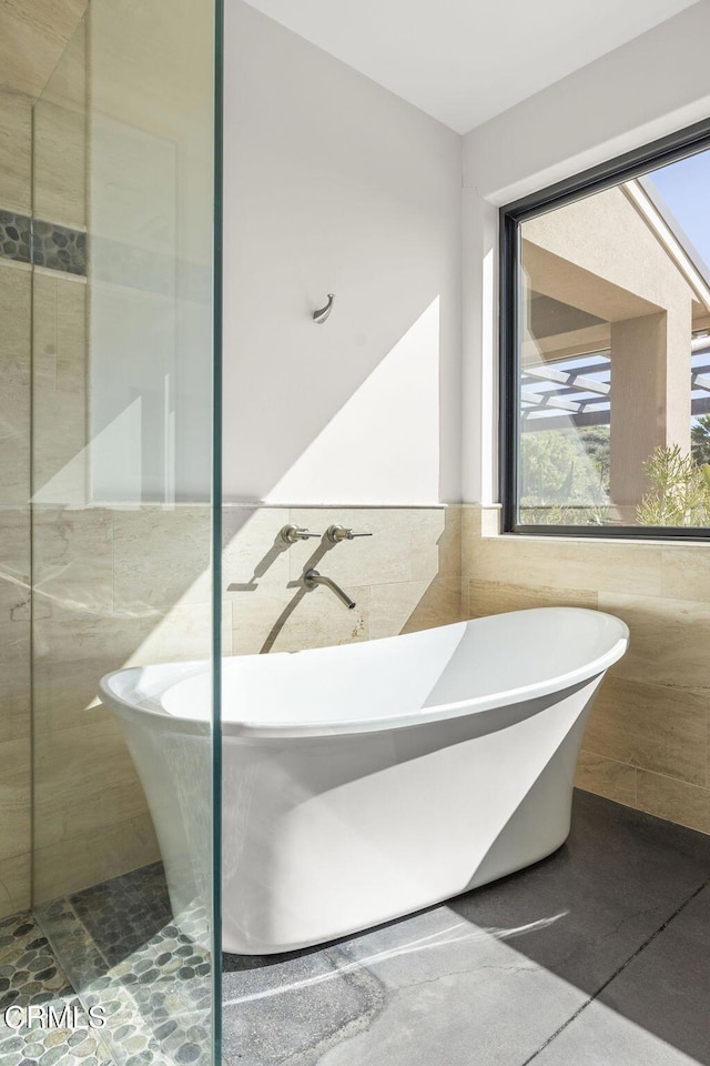 bathroom featuring a soaking tub, a walk in shower, tile walls, and a wainscoted wall