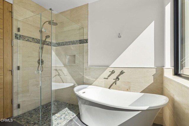 full bath with a soaking tub, tile walls, and a stall shower
