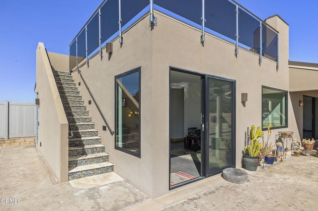 rear view of house featuring stairway, fence, and stucco siding