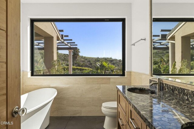 full bath featuring tile walls, toilet, a freestanding tub, tile patterned floors, and vanity