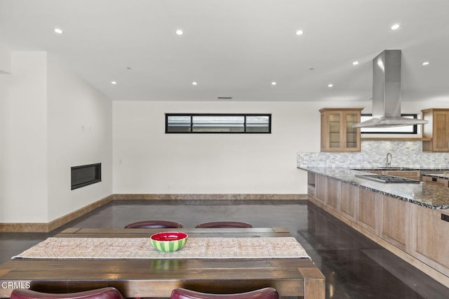 kitchen with decorative backsplash, recessed lighting, island range hood, a glass covered fireplace, and stone countertops