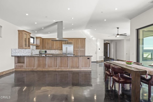 kitchen featuring island exhaust hood, stone countertops, built in fridge, and a sink