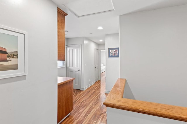 corridor with recessed lighting, light wood-style flooring, attic access, and baseboards