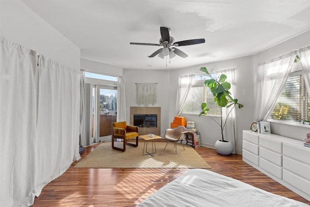 living area featuring a healthy amount of sunlight, a tile fireplace, a ceiling fan, and wood finished floors