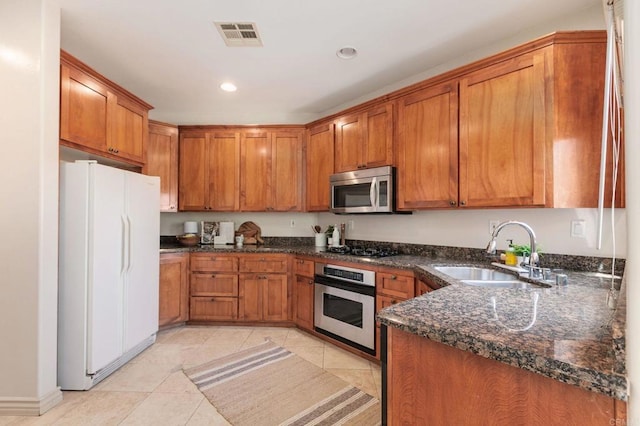 137 Jupiter St, Encinitas, CA 92024 - kitchen featuring appliances with stainless steel finishes, brown cabinetry, light tile patterned floors, dark stone countertops, and recessed lighting