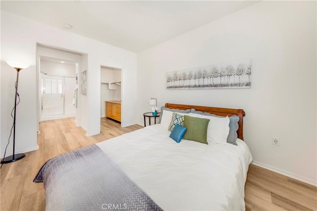 bedroom featuring ensuite bath, a spacious closet, baseboards, and light wood-type flooring