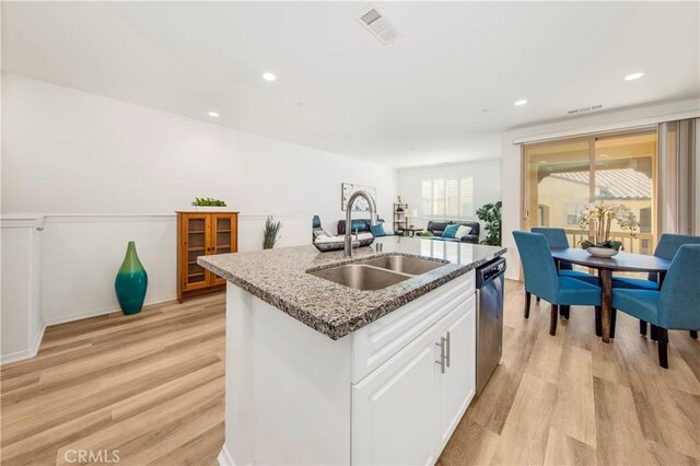 kitchen with visible vents, a sink, light wood-style floors, light stone countertops, and dishwasher