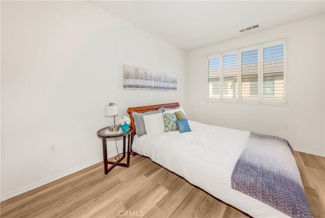 bedroom with wood finished floors, visible vents, and baseboards