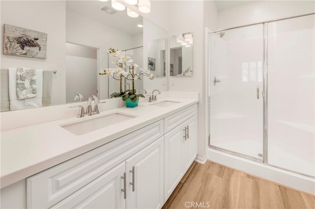 full bath featuring double vanity, wood finished floors, a stall shower, and a sink