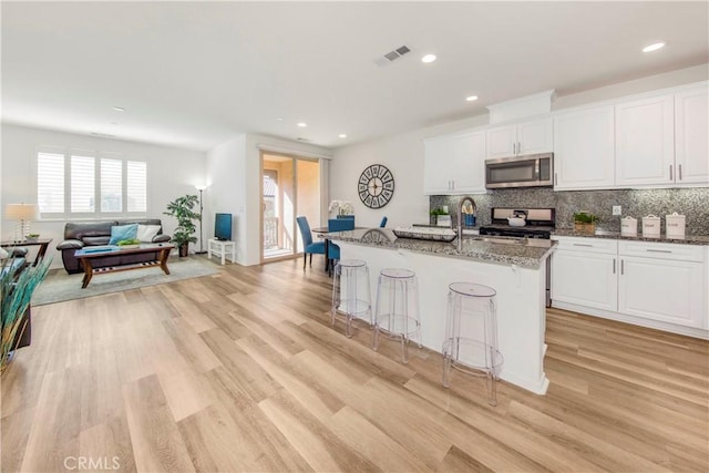 kitchen with visible vents, dark stone counters, stainless steel microwave, range, and backsplash