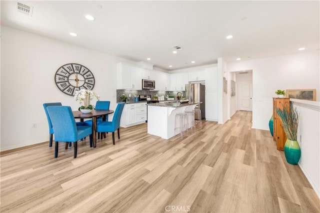 kitchen featuring visible vents, stainless steel appliances, white cabinetry, light wood-type flooring, and a kitchen bar