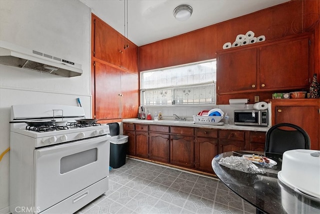 kitchen with a sink, stainless steel microwave, under cabinet range hood, light countertops, and white gas range