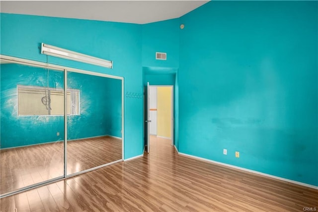 unfurnished bedroom featuring visible vents, wood finished floors, a closet, baseboards, and vaulted ceiling