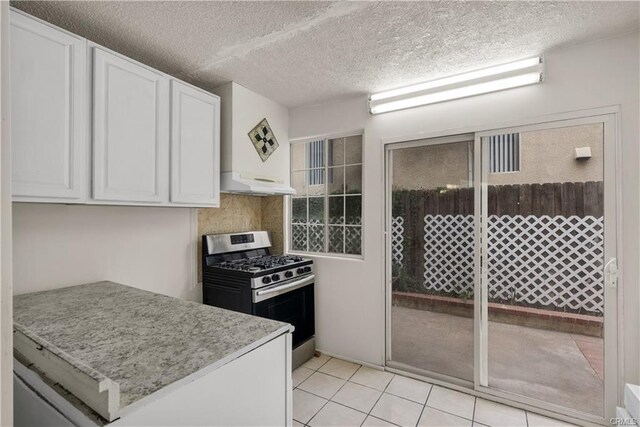 kitchen with white cabinetry, under cabinet range hood, stainless steel range with gas stovetop, light tile patterned floors, and a textured ceiling