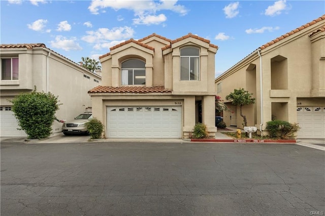 mediterranean / spanish house featuring stucco siding, an attached garage, and a tiled roof