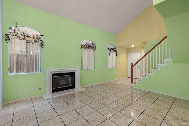 unfurnished living room with a glass covered fireplace, vaulted ceiling, stairway, and tile patterned floors