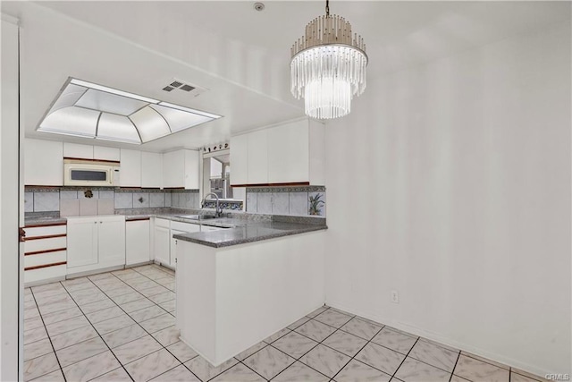 kitchen with white microwave, visible vents, a peninsula, a sink, and white cabinetry