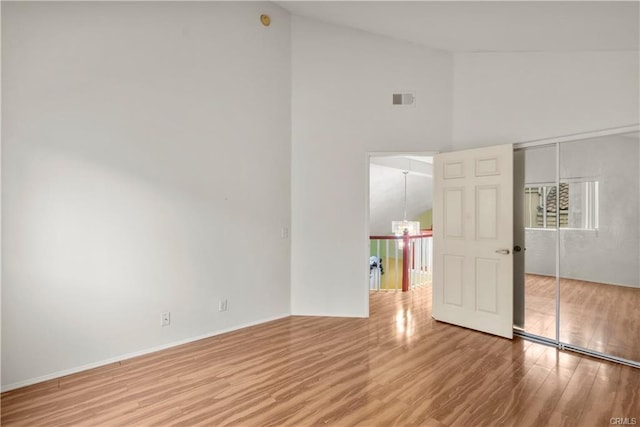 spare room with visible vents, high vaulted ceiling, baseboards, and wood finished floors