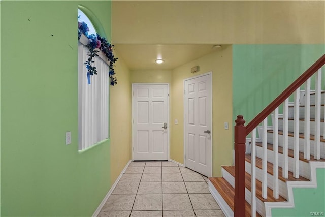 entryway featuring light tile patterned floors, baseboards, and stairs