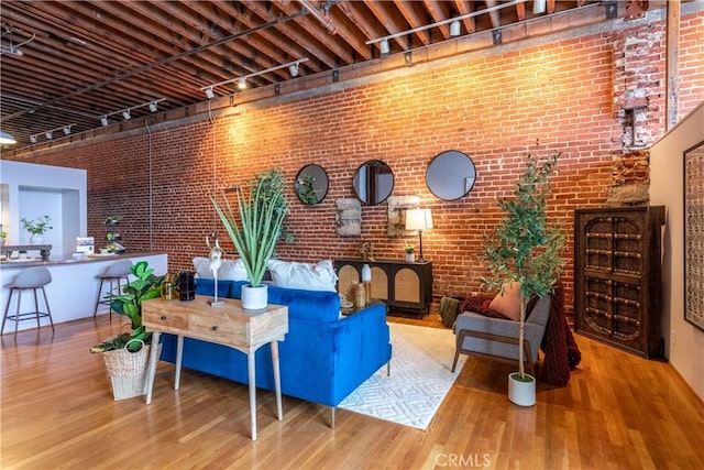 living area with a high ceiling, wood finished floors, and brick wall