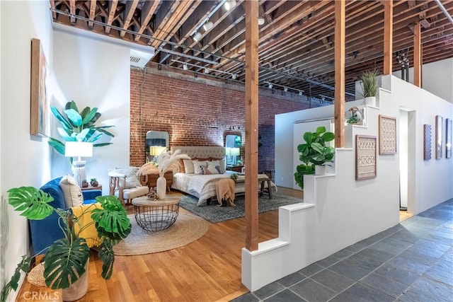 bedroom with visible vents, brick wall, dark wood-type flooring, and a high ceiling