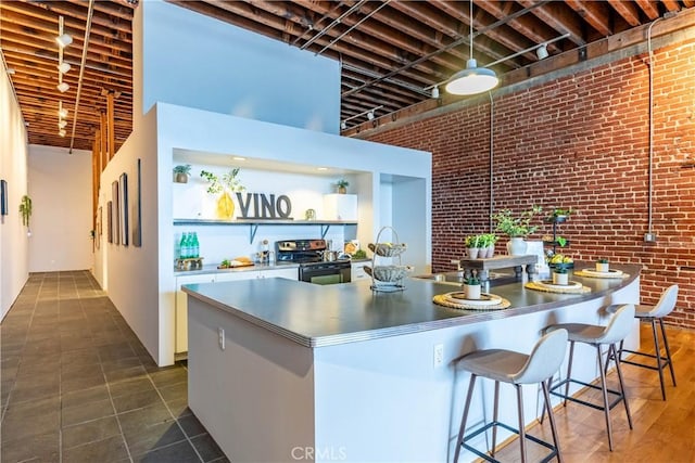 kitchen featuring stainless steel electric range oven, brick wall, open shelves, a high ceiling, and a kitchen bar