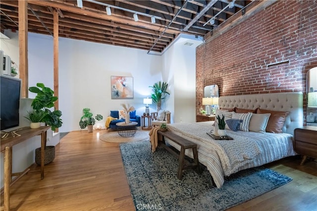 bedroom with brick wall, a high ceiling, and wood finished floors