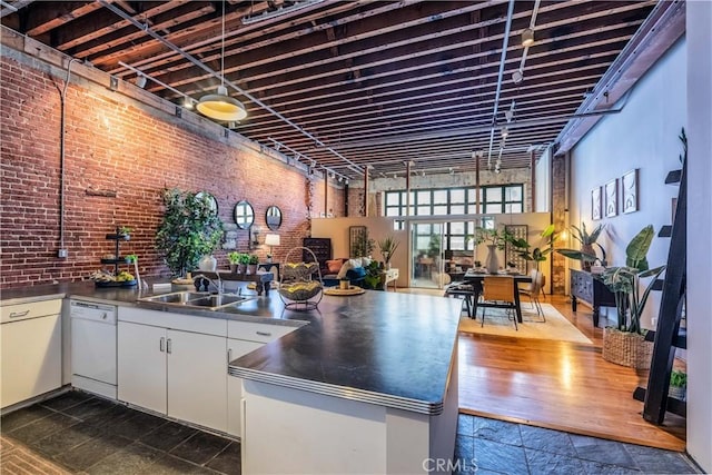 kitchen featuring brick wall, dishwasher, stainless steel counters, a peninsula, and a sink