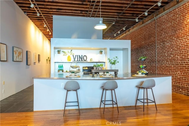 kitchen with wood finished floors, brick wall, a high ceiling, stainless steel counters, and a kitchen breakfast bar