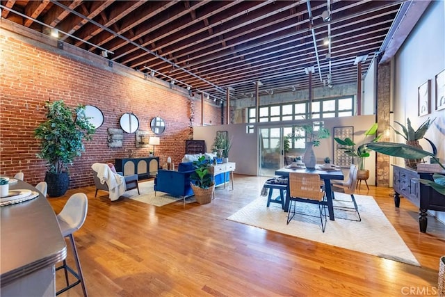 dining space with rail lighting, brick wall, wood finished floors, and a towering ceiling