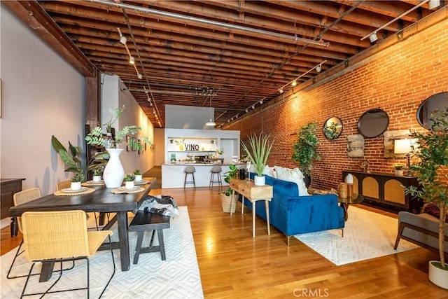 dining space with rail lighting, wood finished floors, and brick wall