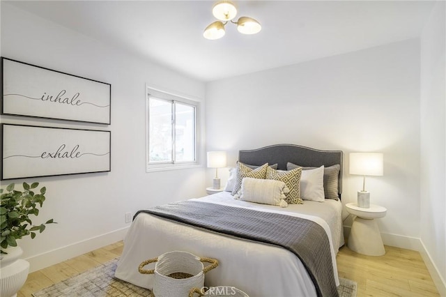 bedroom with an inviting chandelier, baseboards, and wood finished floors