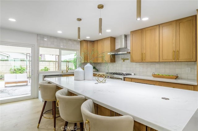 kitchen with pendant lighting, tasteful backsplash, a kitchen island, stainless steel gas stovetop, and wall chimney range hood