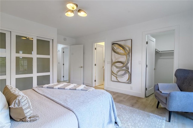 bedroom with a closet, baseboards, a walk in closet, and light wood-style floors