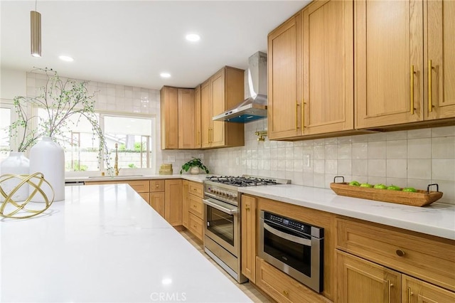 kitchen featuring tasteful backsplash, wall chimney range hood, recessed lighting, high end stainless steel range oven, and a sink