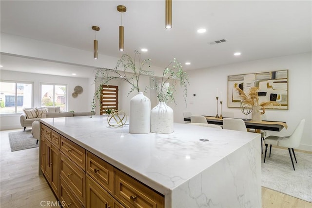 kitchen featuring brown cabinetry, visible vents, light wood-type flooring, recessed lighting, and open floor plan