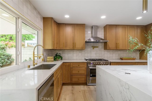 kitchen featuring backsplash, light stone counters, appliances with stainless steel finishes, wall chimney exhaust hood, and a sink