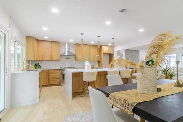 kitchen with visible vents, wall chimney range hood, light countertops, a wealth of natural light, and stainless steel gas stove