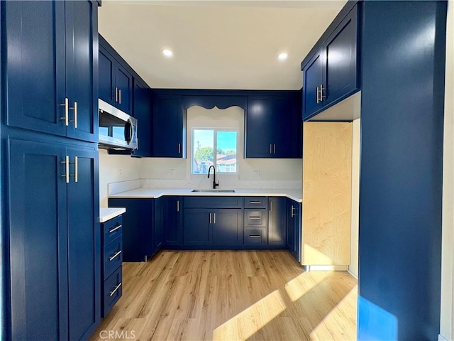 kitchen featuring stainless steel microwave, light countertops, light wood-style floors, blue cabinets, and a sink