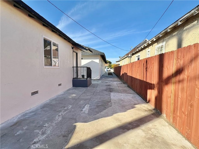 view of side of property featuring a patio area, stucco siding, fence, and crawl space