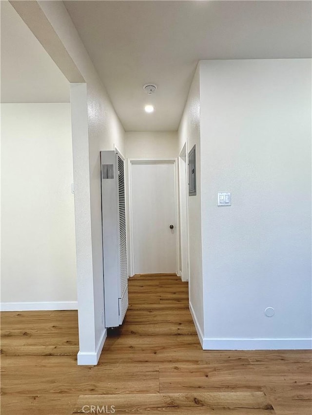 corridor featuring electric panel, a heating unit, light wood-type flooring, and baseboards