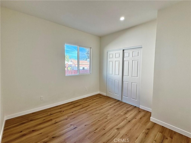 unfurnished bedroom with recessed lighting, light wood-style floors, baseboards, and a closet